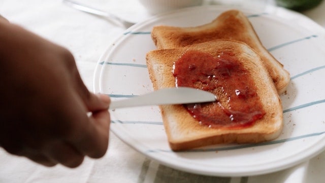 brown hand spreading jam on toast