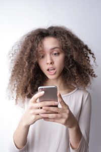 girl with curly hair looks at phone in surprise
