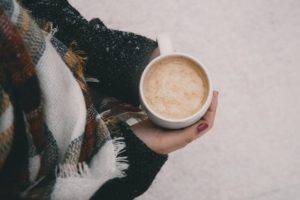 person wearing scarf holding mug of hot chocolate