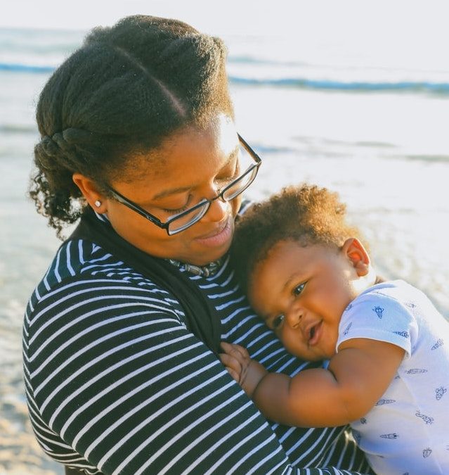 black mother holding baby on the beach