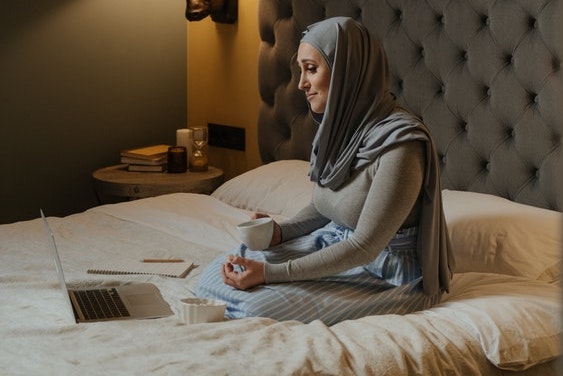 woman with hijab on bed with laptop