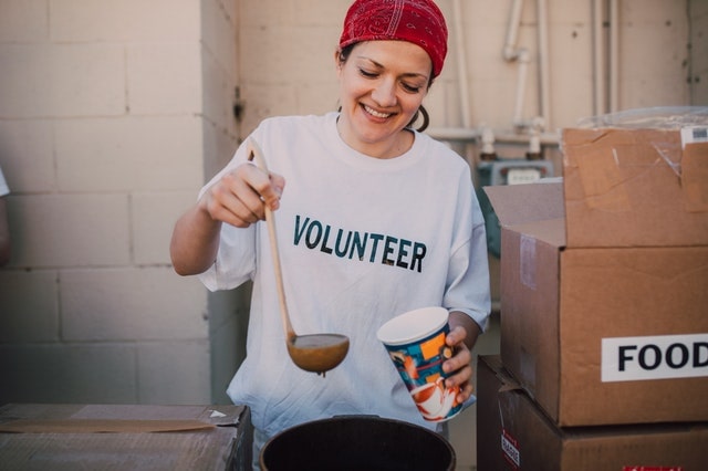 woman with volunteer t-shirt putting soup from a ladle in a cup