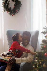 black girl sitting on black man's lap next to a Christmas tree