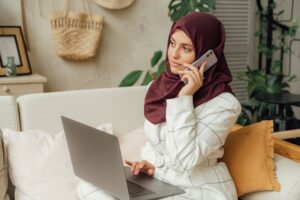 woman with hijab talking on cellphone with laptop on her lap