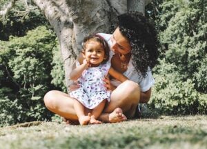 white mother with baby sitting on the grass in front of a tree-therapy for postpartum anxiety